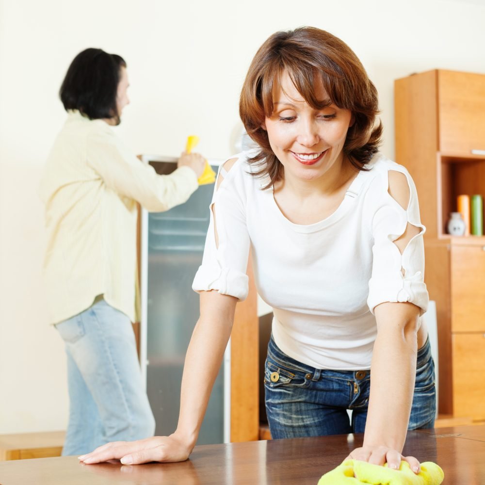 Smiling woman with husband cleaning wooden furiture with rag at home